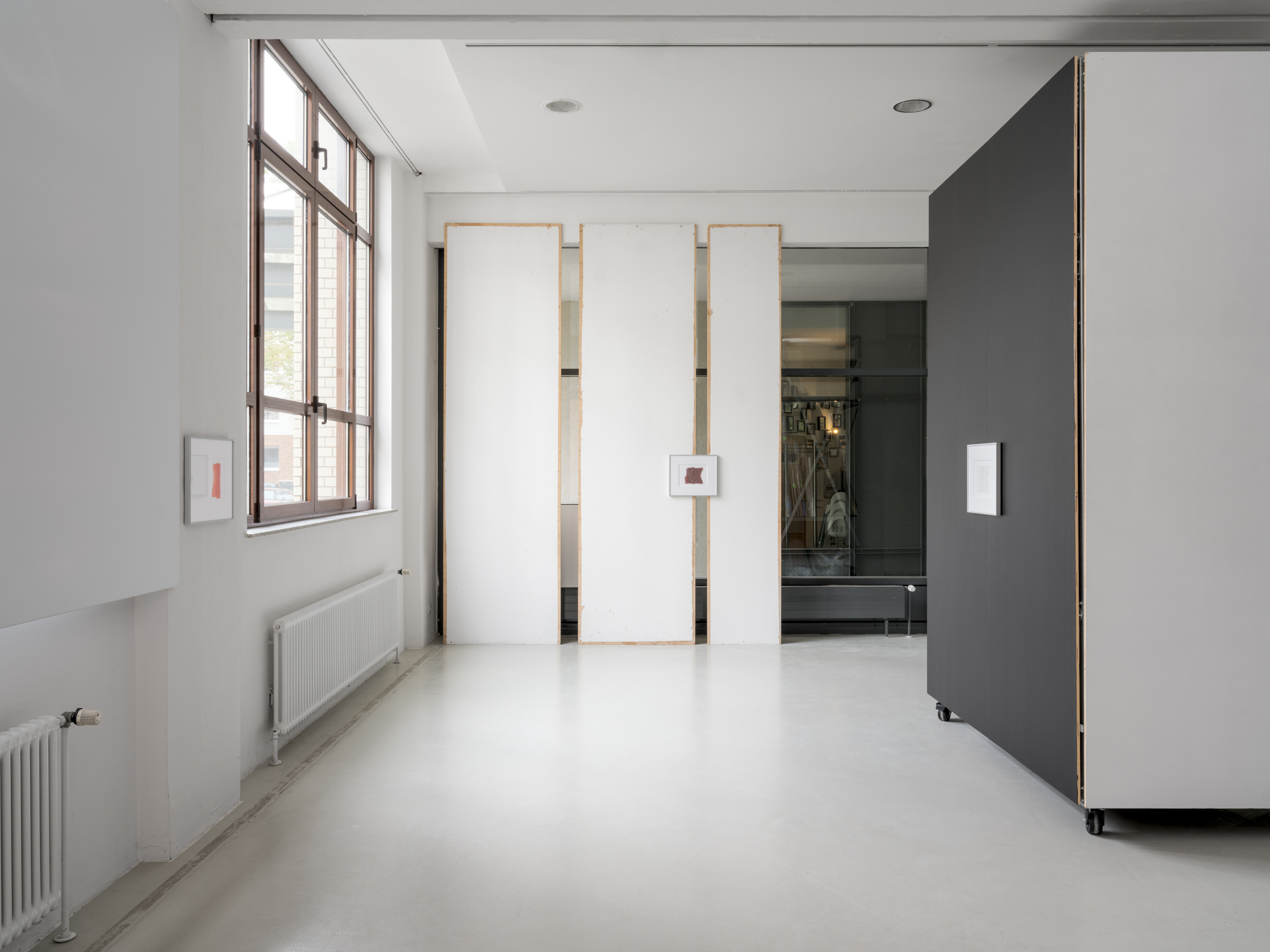 Aisha Altenhofen solo exhibition at Austin Space: Installation view of a minimal white gallery space with grey wooden floors, featuring small framed photographic works and a horizontal industrial light fixture mounted across a central window.